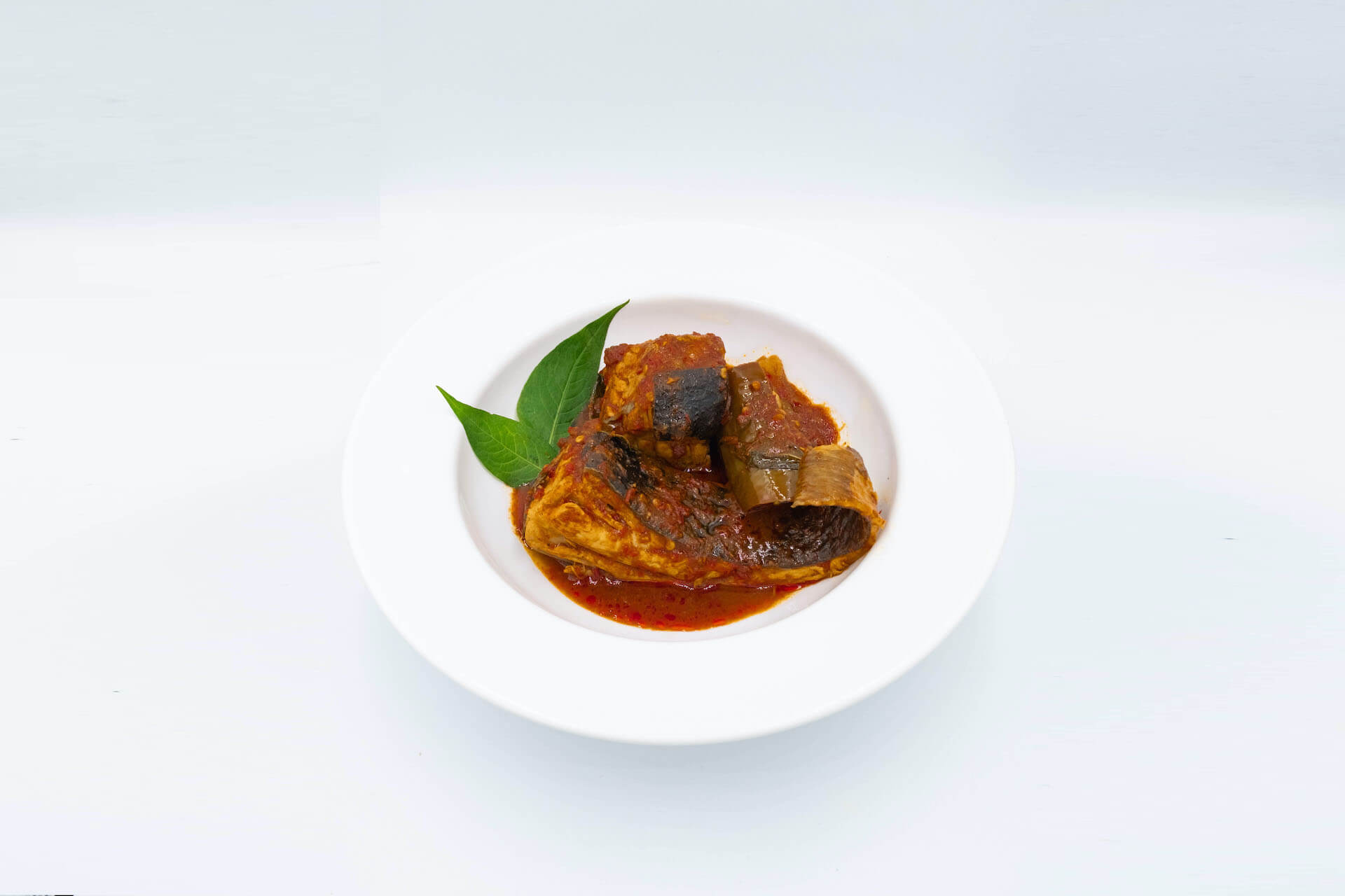 Asam Pedas fish in red sauce with a basil leaf in a white bowl