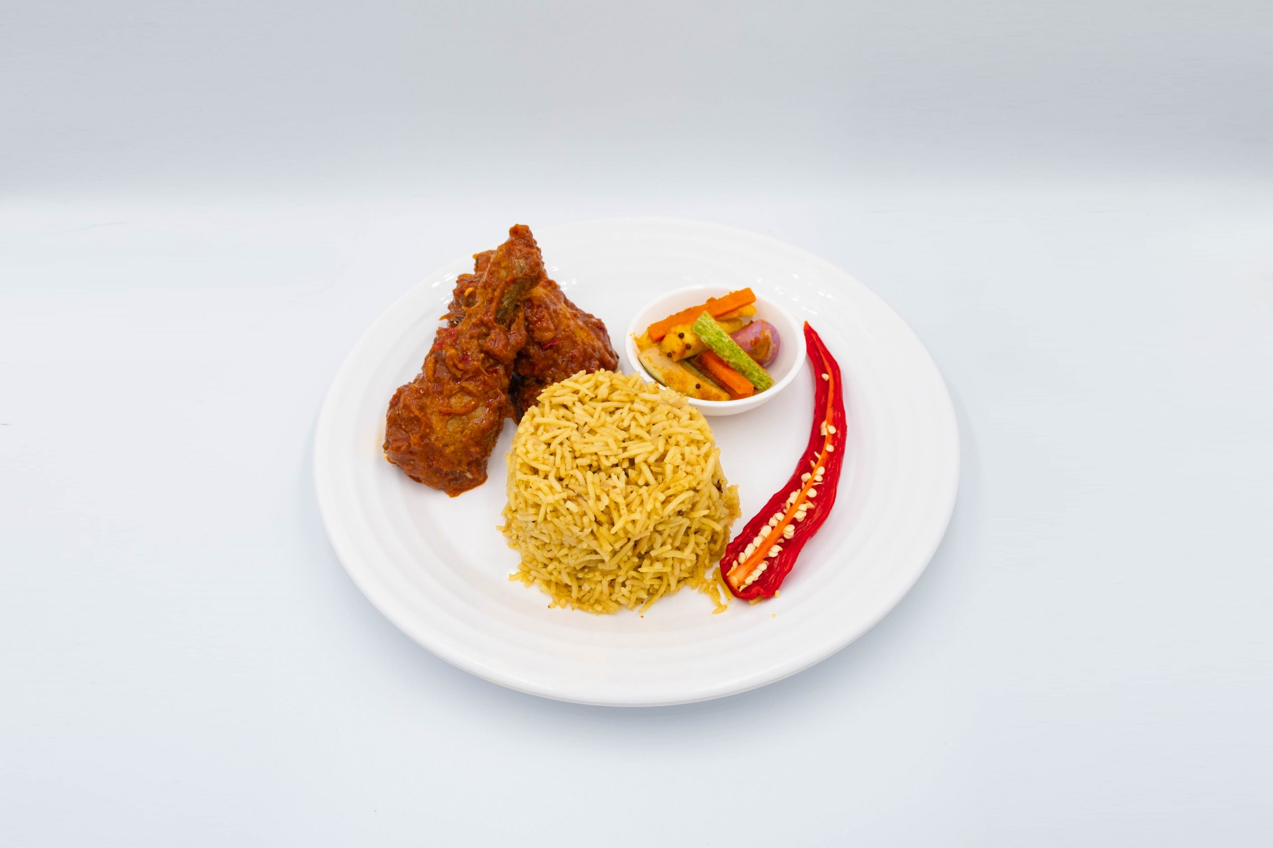 Nasi Minyak with Ayam Masak Merah, acar pickle and red chilli on a white plate